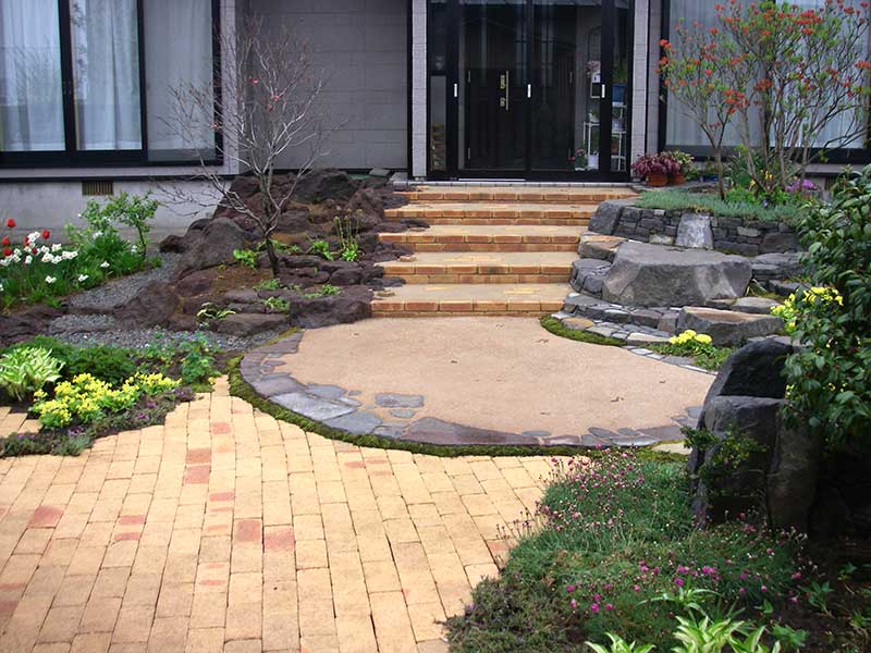 玄関ポーチへ上がる階段の左側は溶岩のロックガーデン、右側は棚田式の花壇